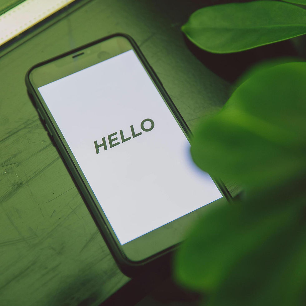 Smartphone on a dark green surface with a plant nearby displays the word "HELLO" on the screen.