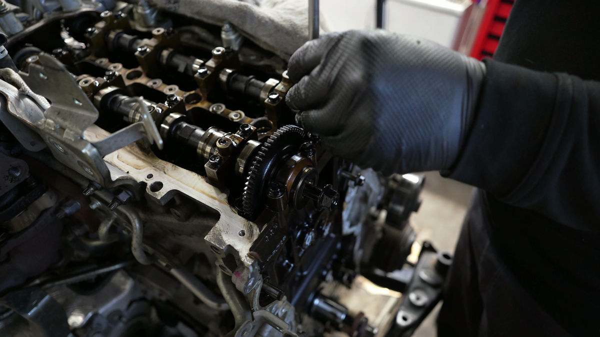 Gloved hands working on an engine's camshaft and timing gear