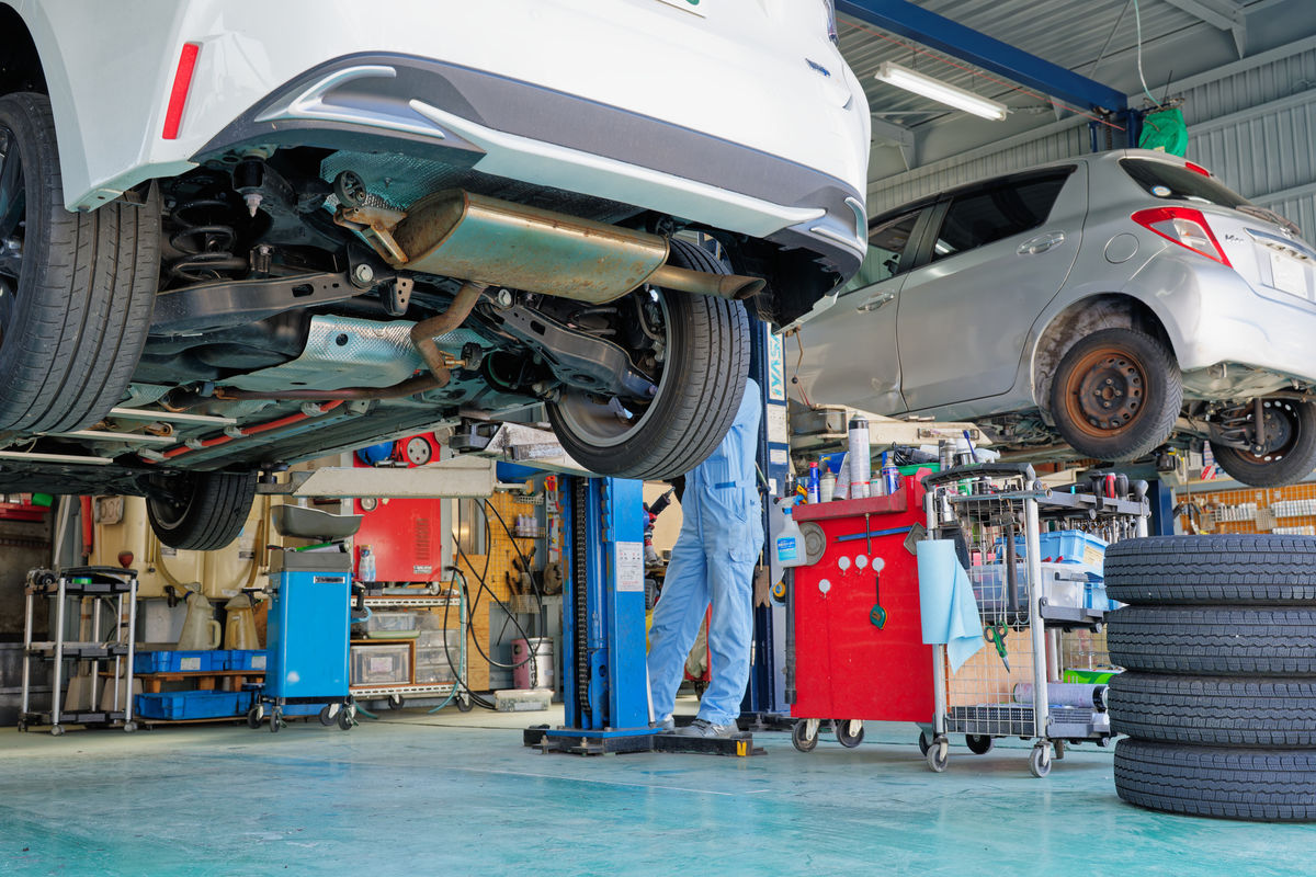 Car raised on a lift in a workshop bay with a mechanic underneath