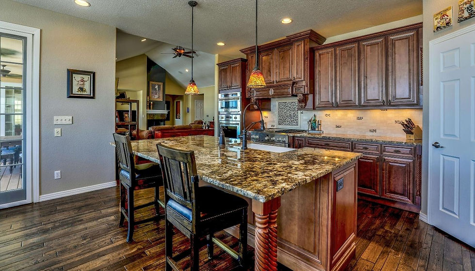 Warm kitchen with granite island, wooden cabinets, and pendant lights. Open living room in the background, creating a cozy atmosphere. Salt to Summit Construction & Renovation in Hyde Park Utah