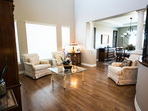 Bright Providence Utah living room with beige armchairs, glass coffee table, and lamp. Wooden floor, dining area in background, decorative plants visible.