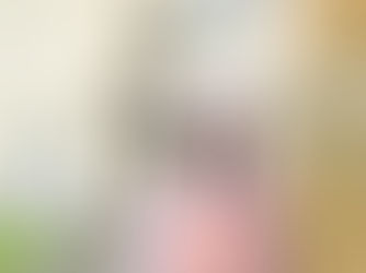 Jo stands outside an old building. She wears a pink woolly hat, coral T-shirt and a pink coat.