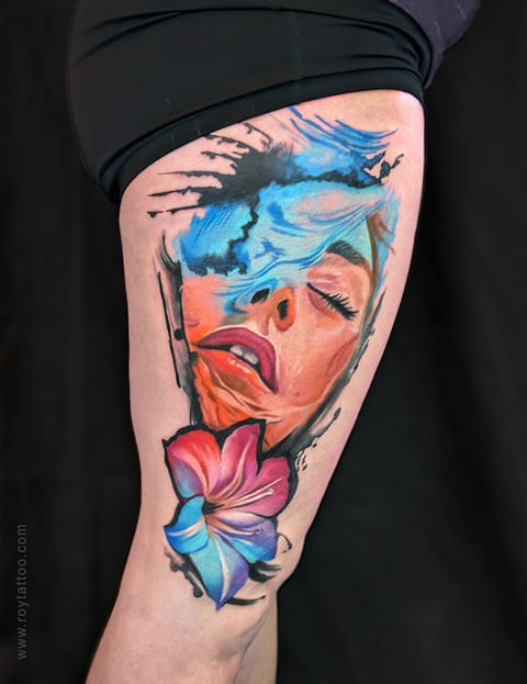A large color realism thigh tattoo by artist Sushmita Roy, featuring a woman’s face with expressive eyes closed, blue hair strokes blending into abstract textures, and a vivid pink-and-blue flower beneath her chin. Winner of Best Large Color Tattoo 2025 at Digby Inktoberfest.