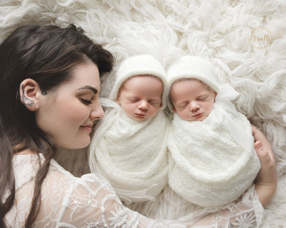 Mother lying beside twin newborns swaddled in white wraps