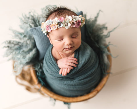 Newborn baby girl sleeping in teal wrap with floral headband in basket