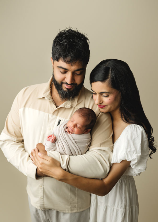 Parents holding newborn baby wrapped in neutral blanket