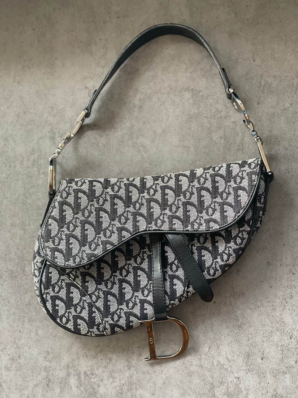 Top-down view of Dior Saddle Bag in black and grey monogram canvas displayed flat, showing full shape and flap design.
