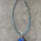 Thumbnail: Square Glass Flower Pendant Necklace full top view showing teal cord & dark floral pendant with bold blue flower contrast