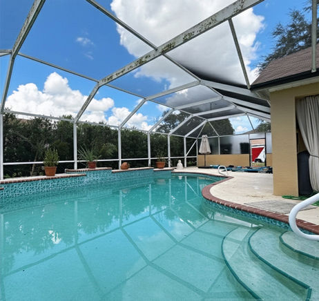 Before photo of a pool cage with mold on the frame and damaged screens surrounding the pool.