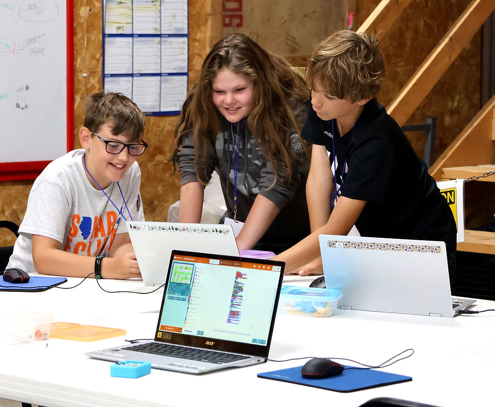 Three young teens smile and stand around a laptop computer looking at a game they coded.