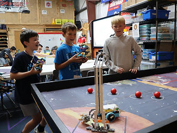 Two LEGO robots face off in a "demolition derby" type-game on a square game table with students watching on.