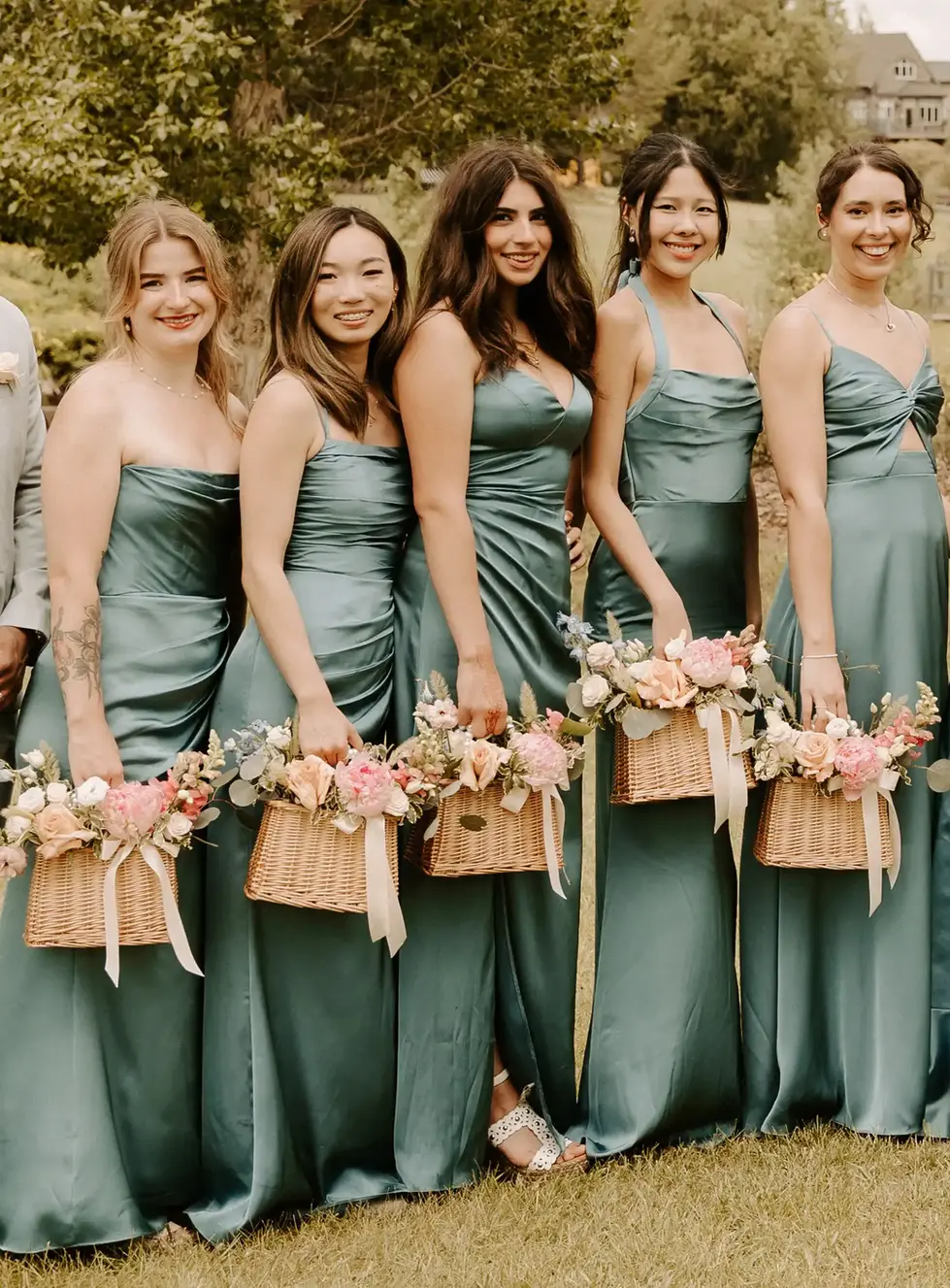 Bridesmaids in sage green satin gowns holding floral baskets