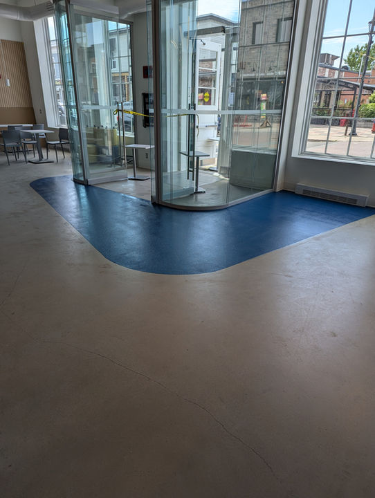 Porte tournante en verre moderne, sol beige clair avec motif bleu.