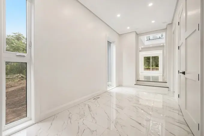 Empty white room with marble floors and natural light from tall windows.