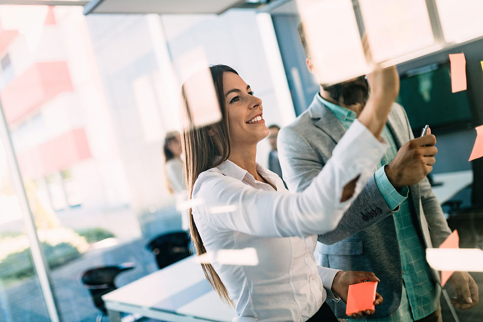 Smiling woman placing sticky note on glass wall during team meeting.