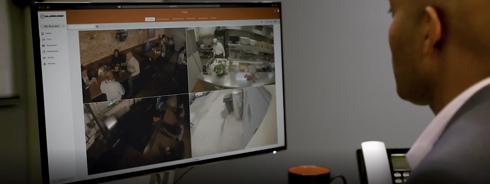 Man monitoring security cameras, COMMERCIAL SECURITY SYSTEMS, with multiple live feeds actively displayed.