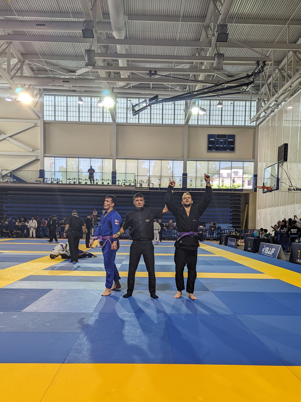 Trois athlètes posant sur tatami bleu et jaune, bras levés.