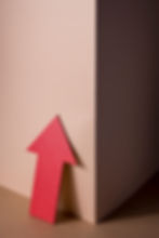 Red arrow pointing upwards, leaning against a light wall with shadow.