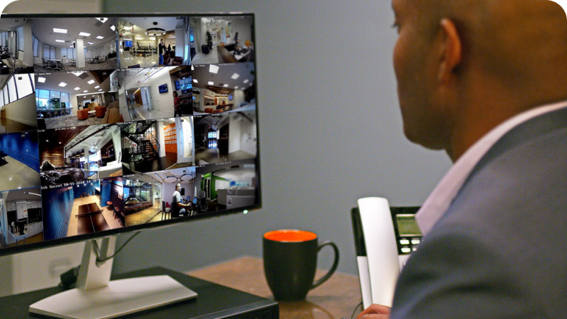 Man monitoring security cameras, offices visible on the large display, alarm monitoring.