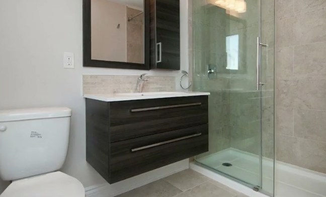 Modern bathroom with dark wood vanity, glass shower, and white toilet