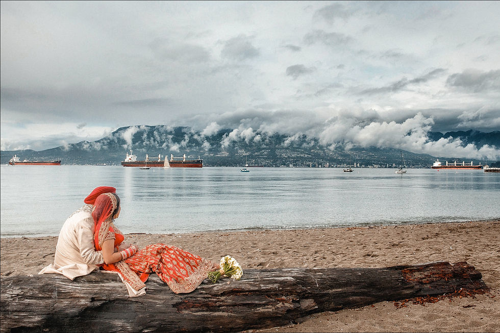 Indian couple sits on the log with mountains, harbor and multiple ships in the background