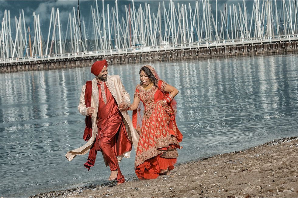 Indian bride and groom run down the beach with yachts and mountains in the background