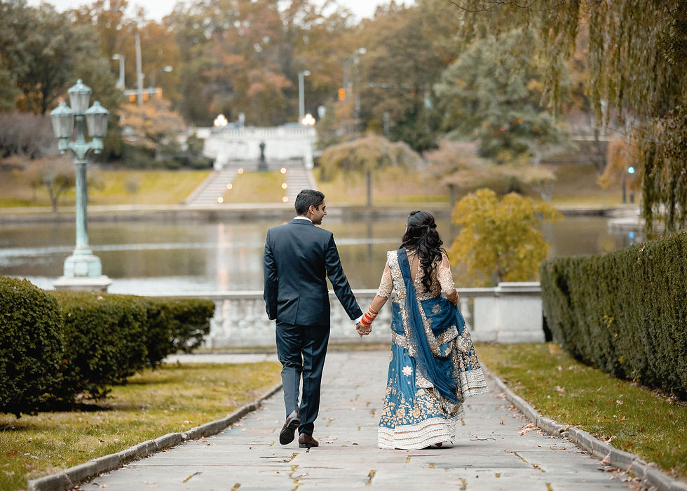 newlyweds hold hands and walk away down the path that leads to a lake