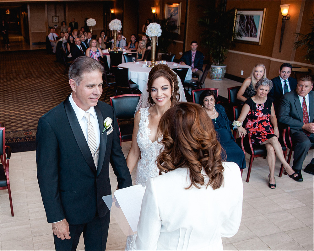 Shot of bride and groom with guests in the background over the officiants shoulder at Marriott Key Tower.