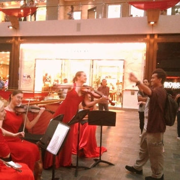 Violinists in red dresses playing in a mall with a man conducting