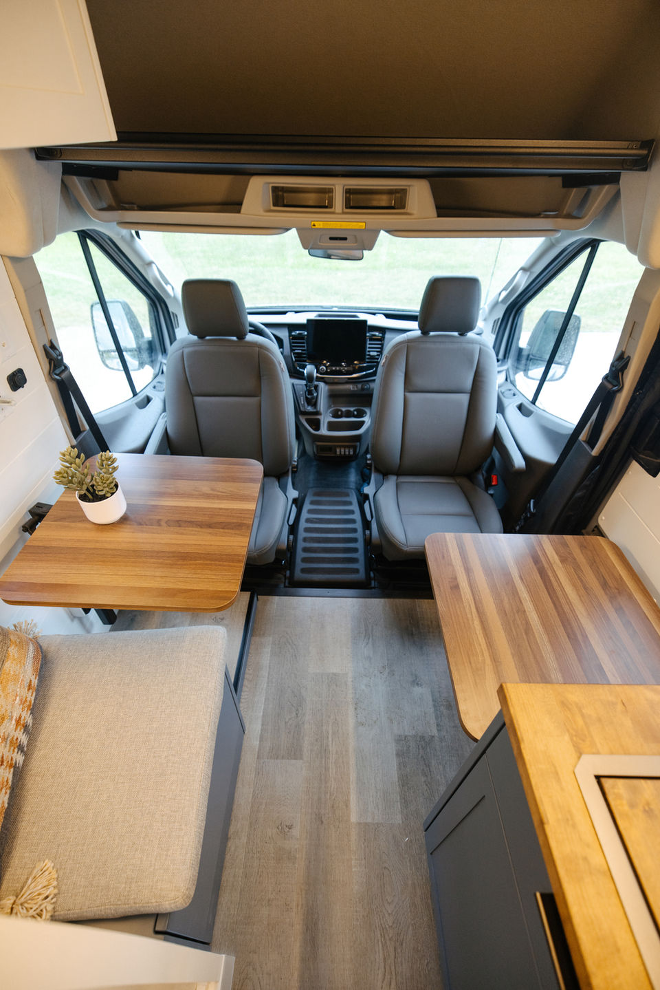 Camper van front seats with folding table and light wood flooring.