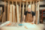 Paul Domish posing in the Drifter Vans workshop, wearing a black tee and leather apron, leaning on the table saw.