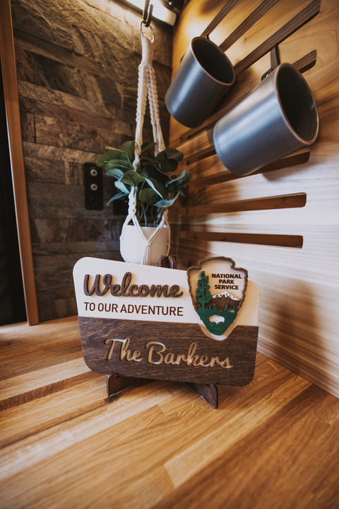 Camper van kitchen counter with wood decor and “Welcome to Our Adventure” sign.