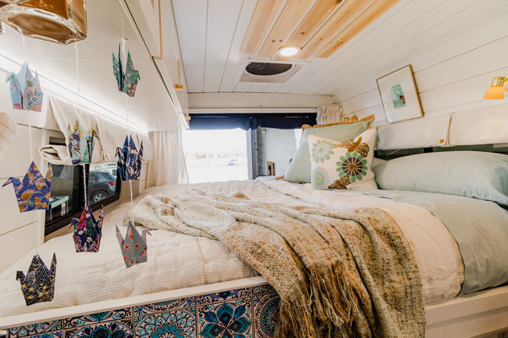 Camper van bed with handmade art hanging above.