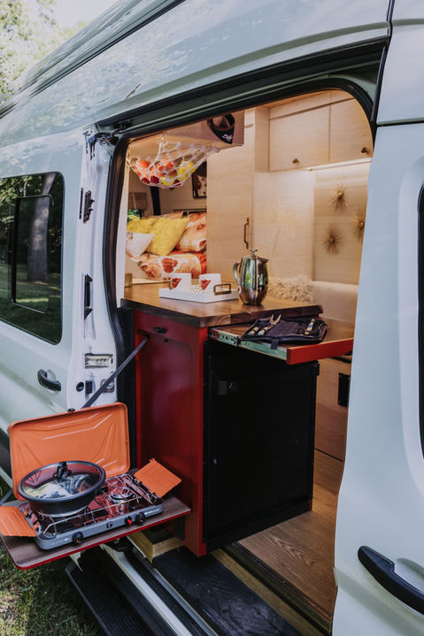 Camper van side door open with outdoor slide-out kitchen drawer.