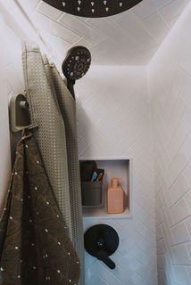 Camper van shower with white tile, black shower head, and storage niche.