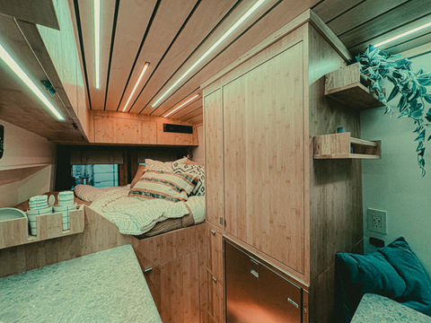 Camper van bed with light wood walls and cozy linens.