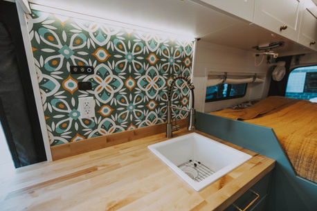 Campervan kitchen in a Drifter Layout featuring a custom backsplash, upper cabinets, and solid-surface countertops.