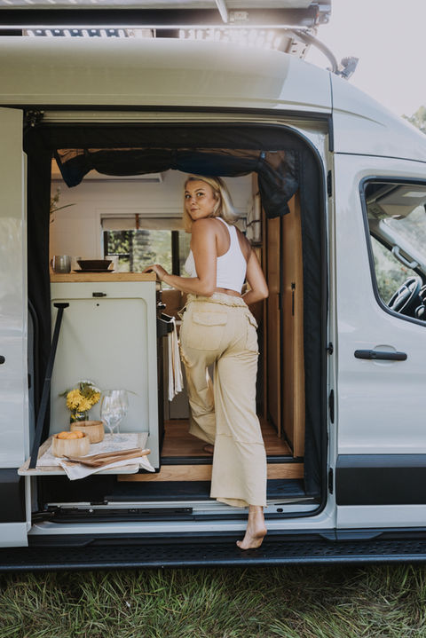 Person standing by open van door, smiling with sunlight streaming in.