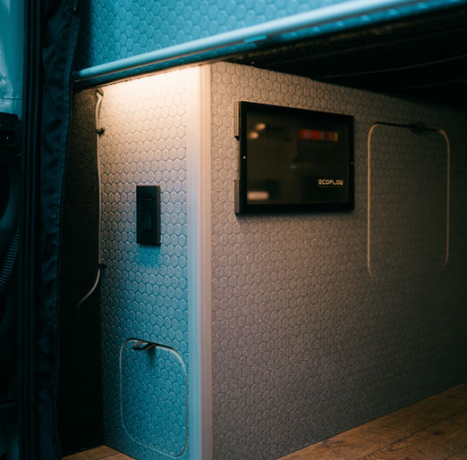 Garage view of the EcoFlow Power Kit installed in a camper van, showing lithium batteries, inverter, and wiring neatly organized beneath the bed platform.