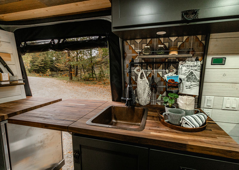 Camper van kitchen counter with bronze sink and potted plant.