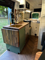 Camper van kitchen with brass sink, walnut counter, and modern fixtures.