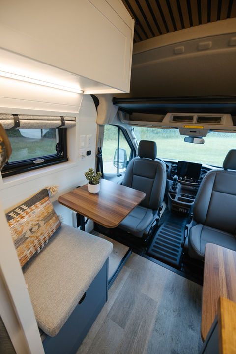 Camper van interior showing dining table and cushioned bench seating.