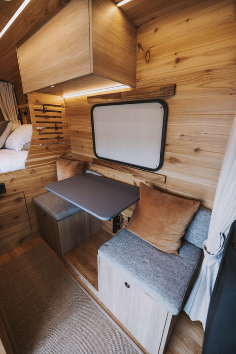 Camper van dinette area with grey cushions and folding table.