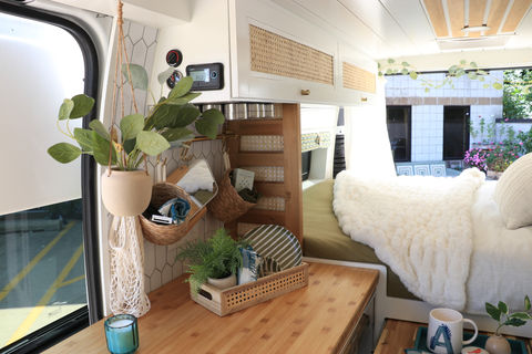 Camper van interior with white walls, wood countertop, and plants.