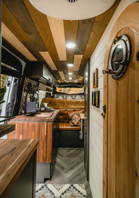 Man smiling inside rustic camper van with wood interior and ambient lighting.