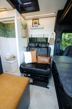 Camper van seating area with black leather seats and fold-out tables.