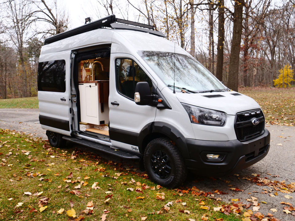 Ford Transit Trail camper van parked on a leaf-covered road.