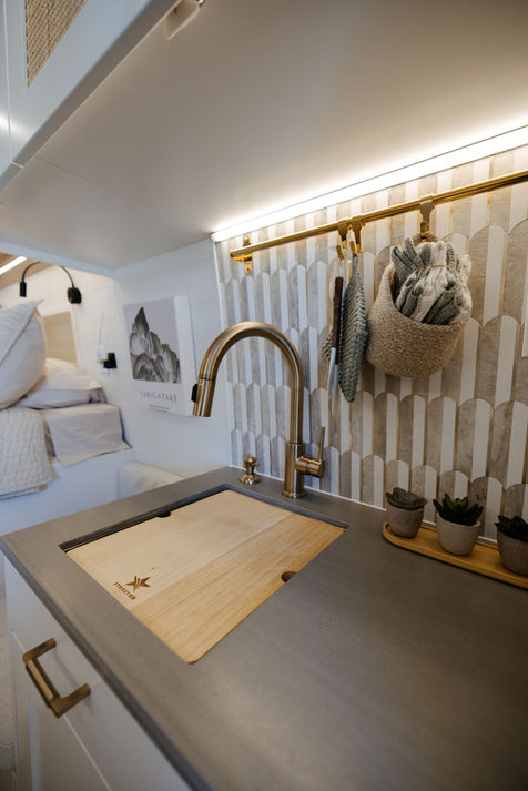Camper van kitchen area with gold faucet and wall hooks.