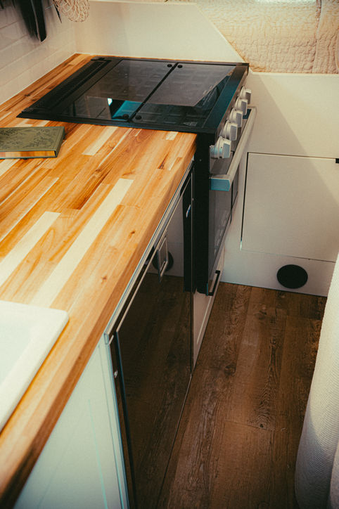 Camper van kitchen with stovetop and wood counter.