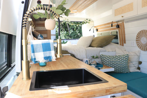 Camper van kitchen sink and faucet with greenery and bright lighting.